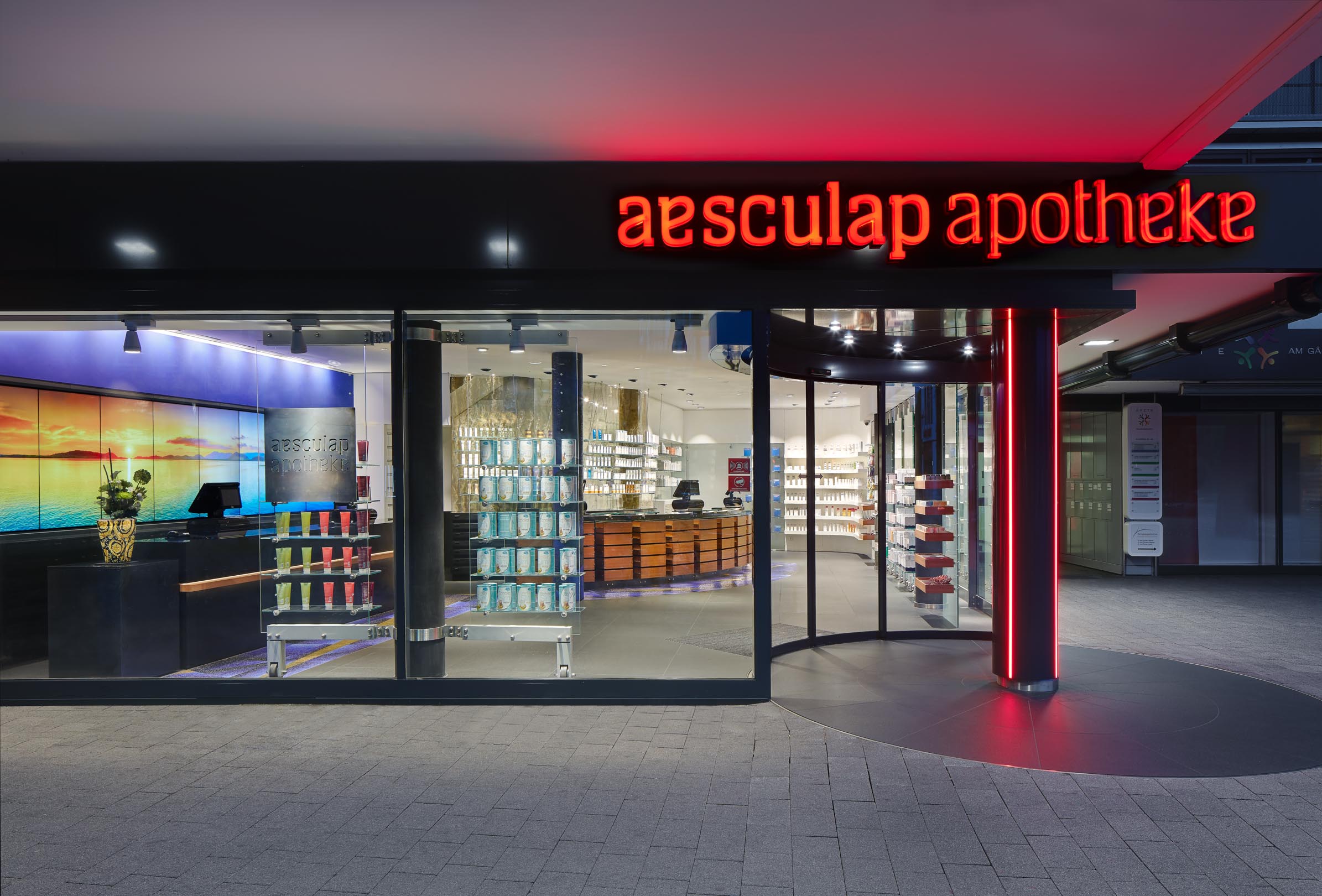 Aesculap Apotheke Neumünster, neuer Eckeingang mit Rundbogen-Automatiktür und LED-beleuchteter Stütze