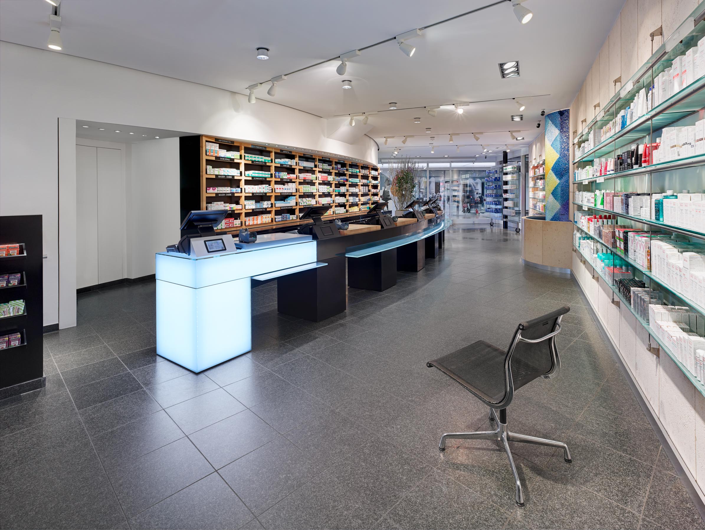 Bright, spacious dispensary with a dark granite floor, curved black prescription counter and full-height medicine display systems