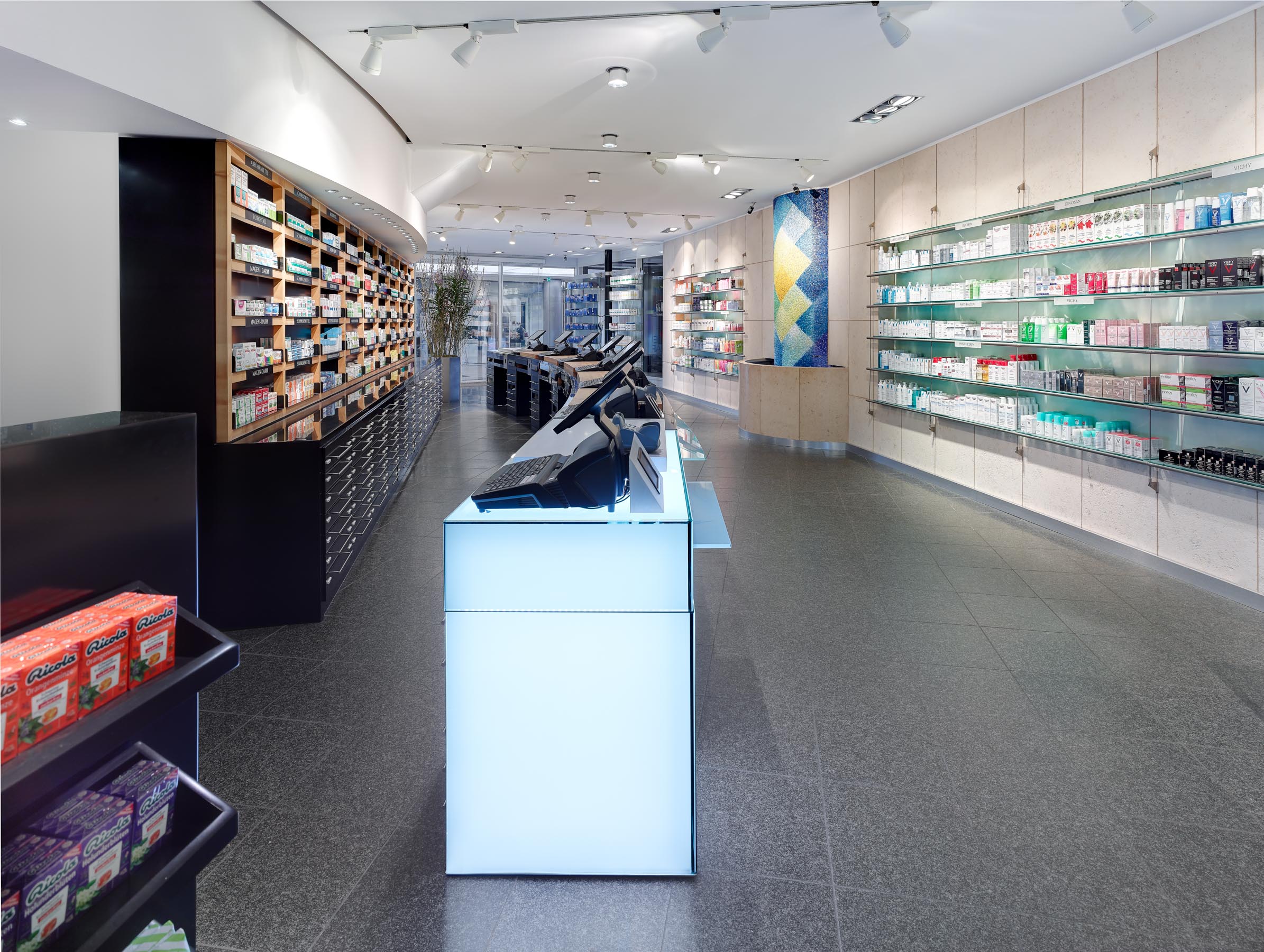 Long view along the illuminated Corian checkout counter towards the structured self-service wall and mosaic fountain