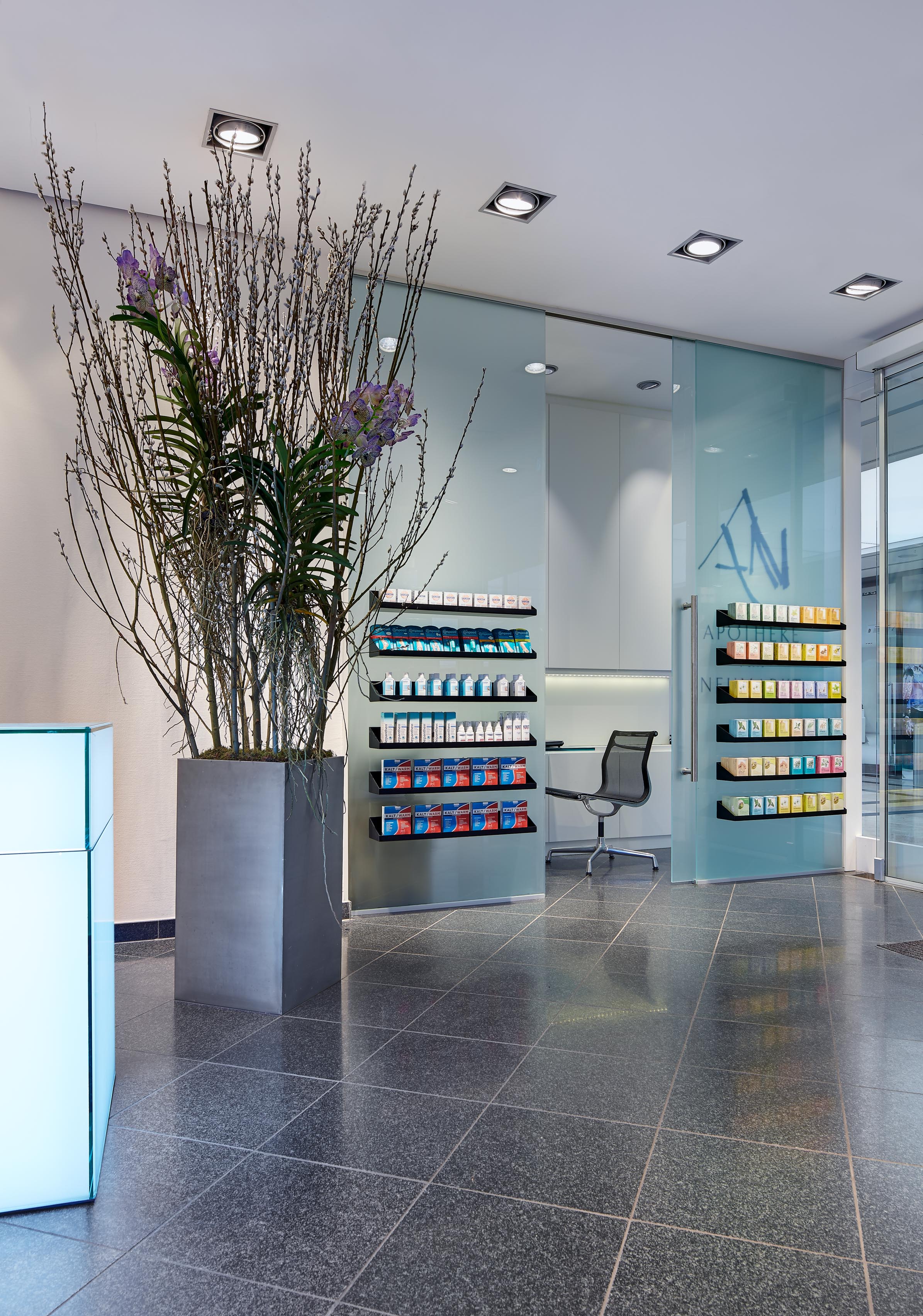 Private consultation area with a frosted-glass sliding door bearing the pharmacy logo and a minimal workstation