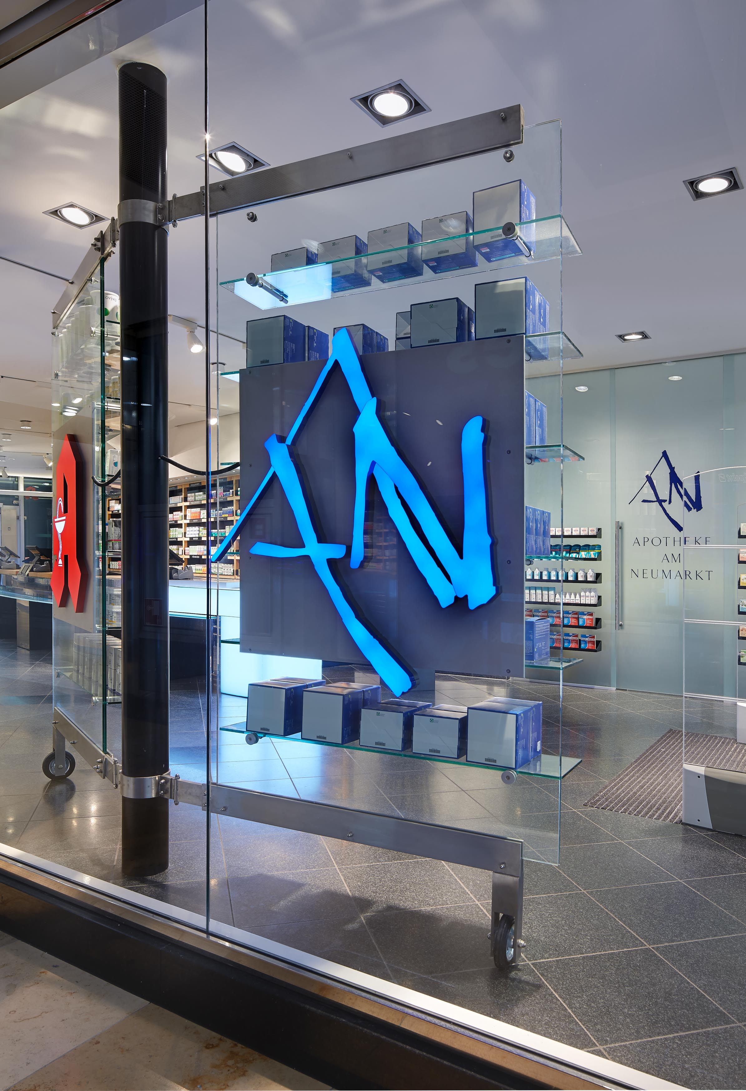 Close-up of the illuminated blue AN logo on a freestanding glass shelving system in the shop window