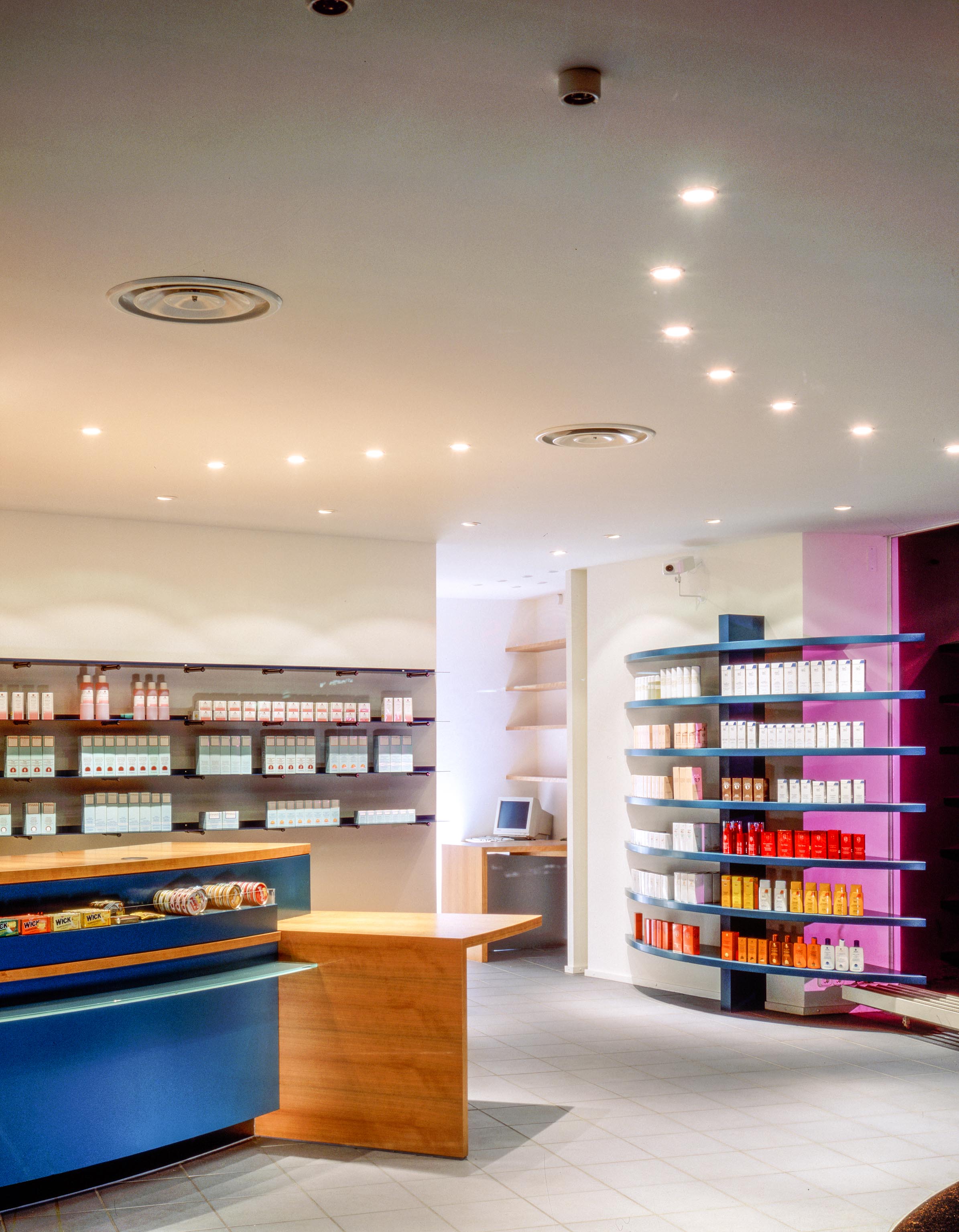 Dispensary with self-service shelving, curved prescription counter and integrated consultation area at the rear