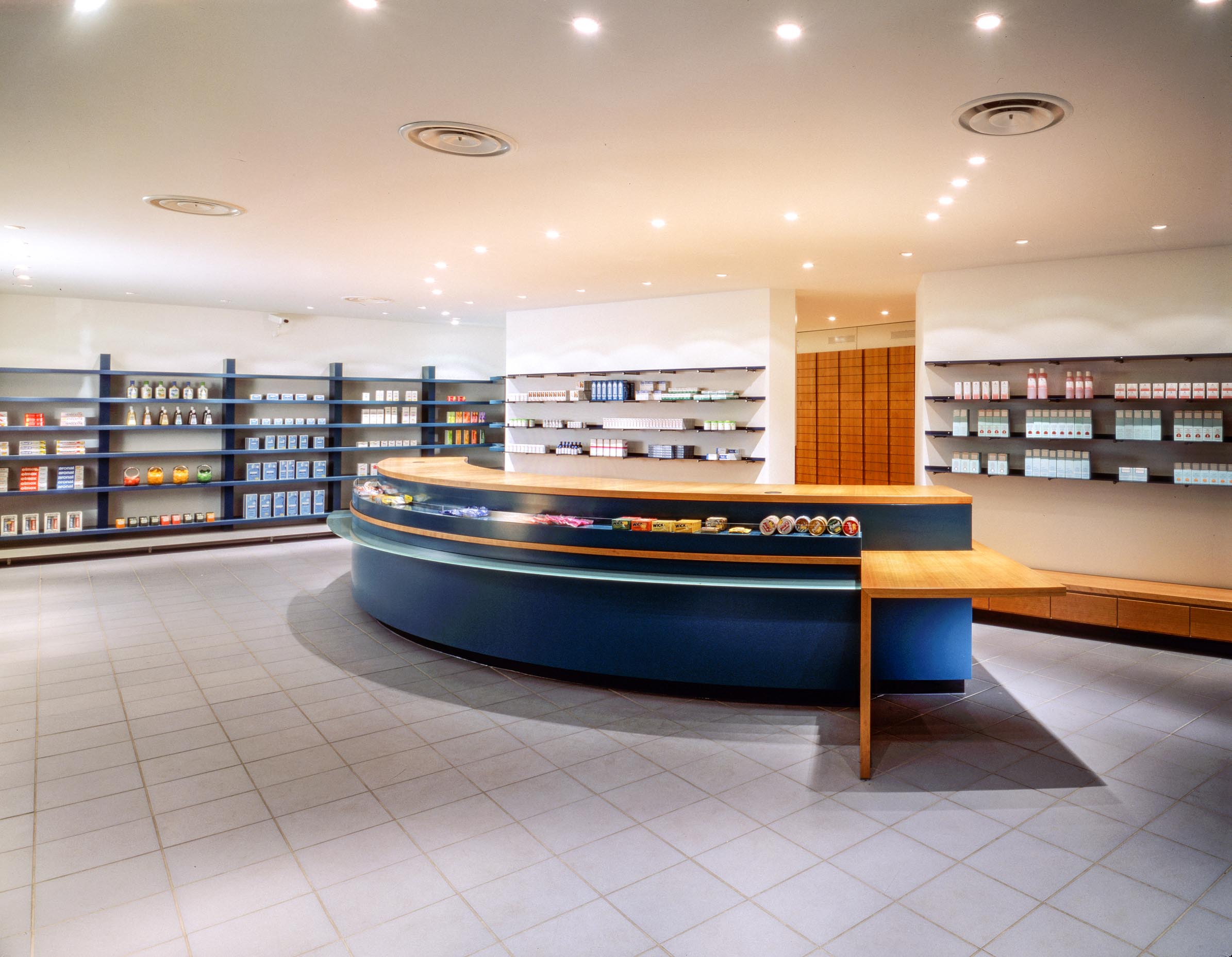 Dispensary with prescription counter and medicine display structured by a large curved counter in blue and wood