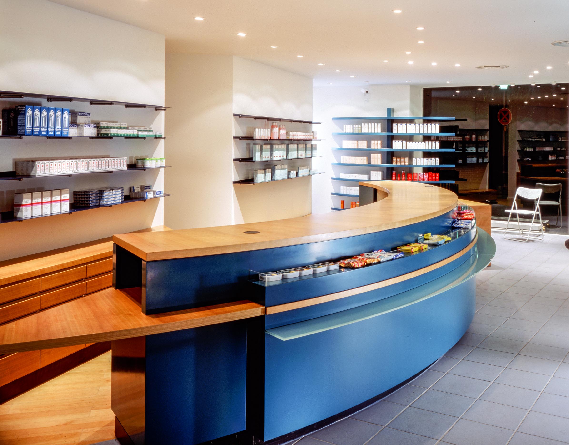 Detail of the prescription area with curved counter, medicine display shelving and bench along the wall