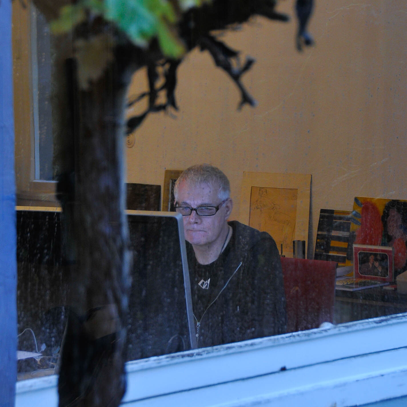 Architect Klaus Bürger working at his computer, photographed through a window of the winter garden