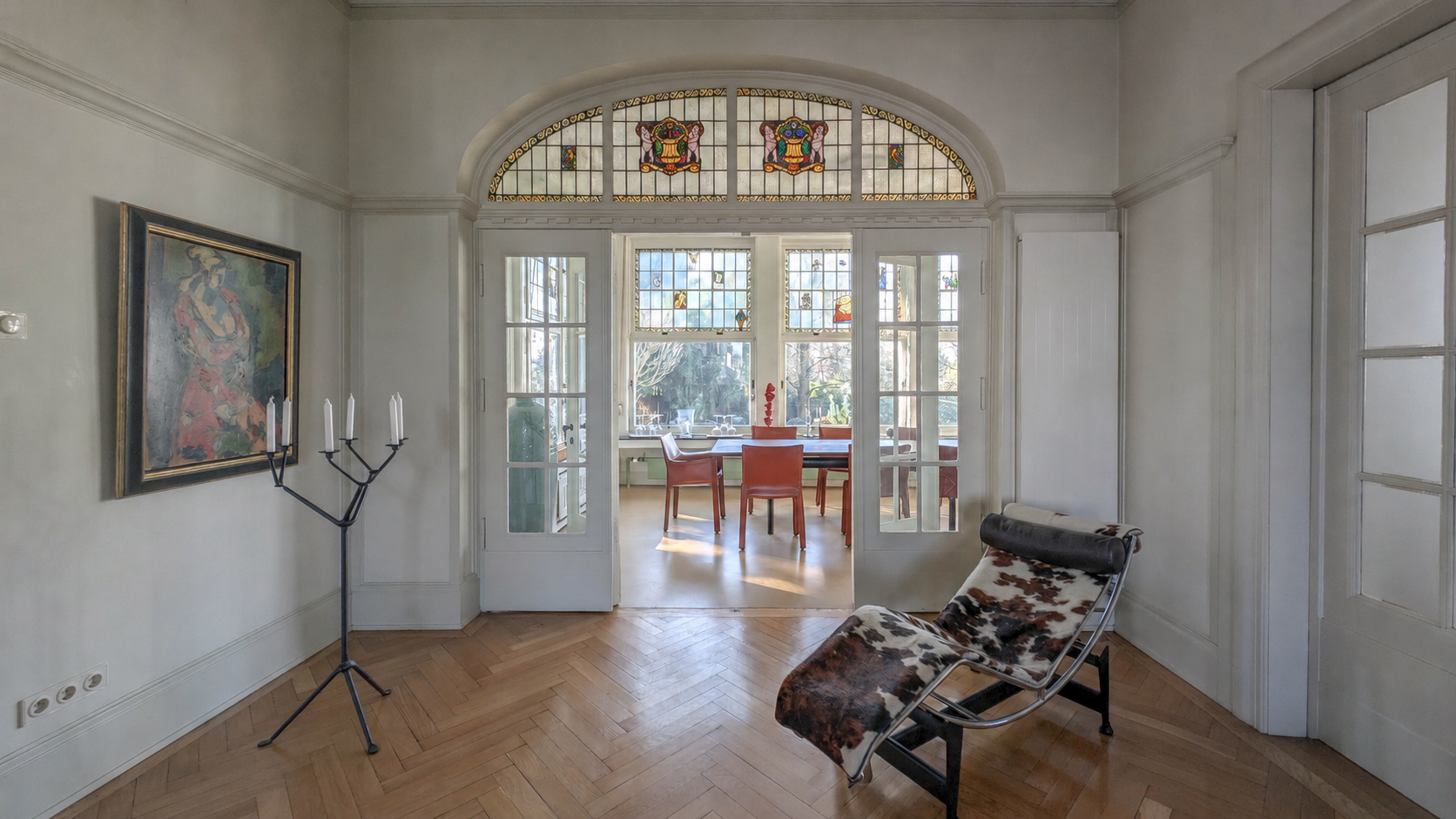 View through an open white double door with a leaded-glass arched fanlight, across the herringbone parquet floor towards the bright meeting area beyond