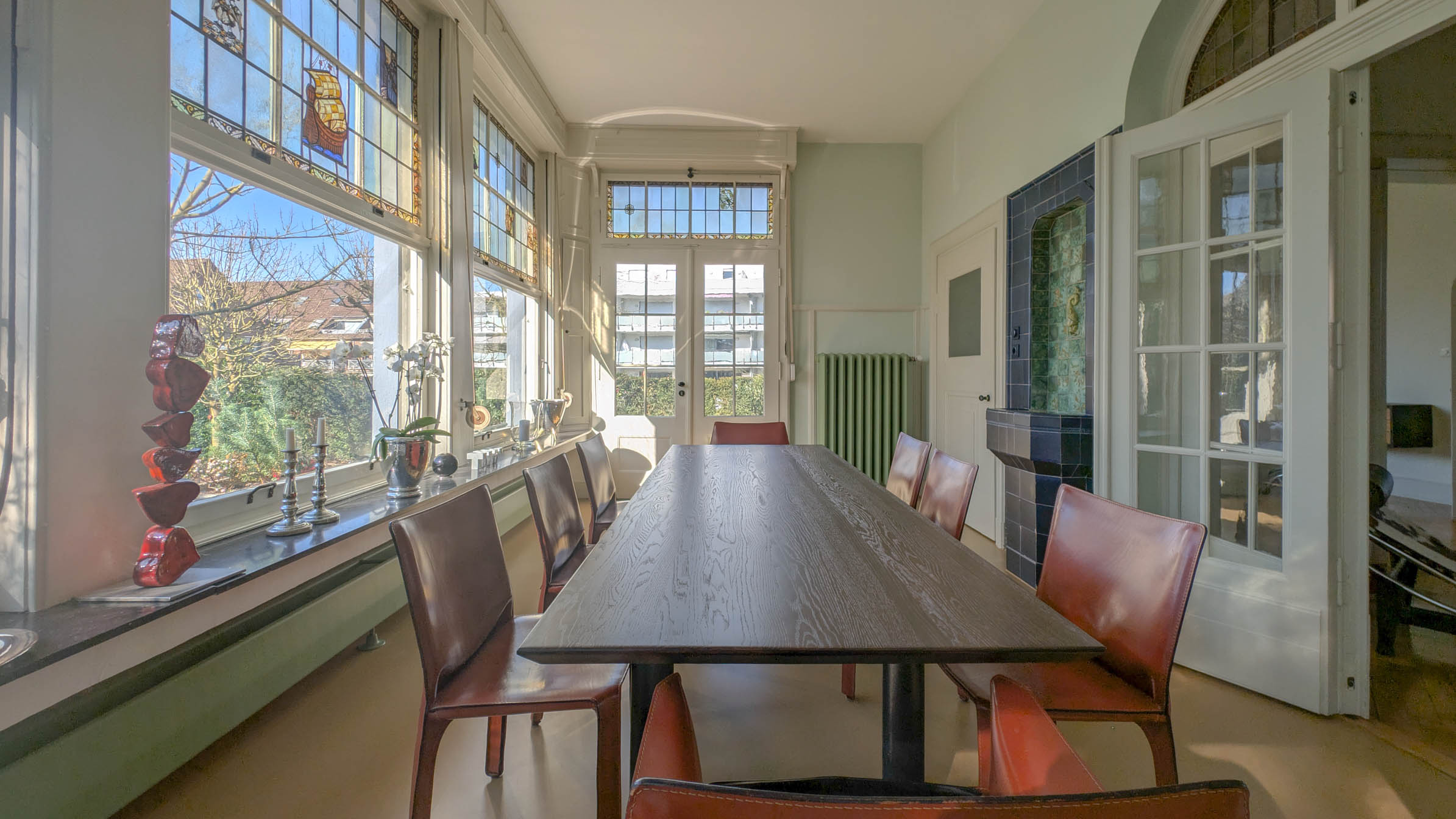 Bright meeting room in the conservatory with a long dark wooden table, leather cantilever chairs, coloured leaded-glass windows and the historic deep-blue tiled wall fountain